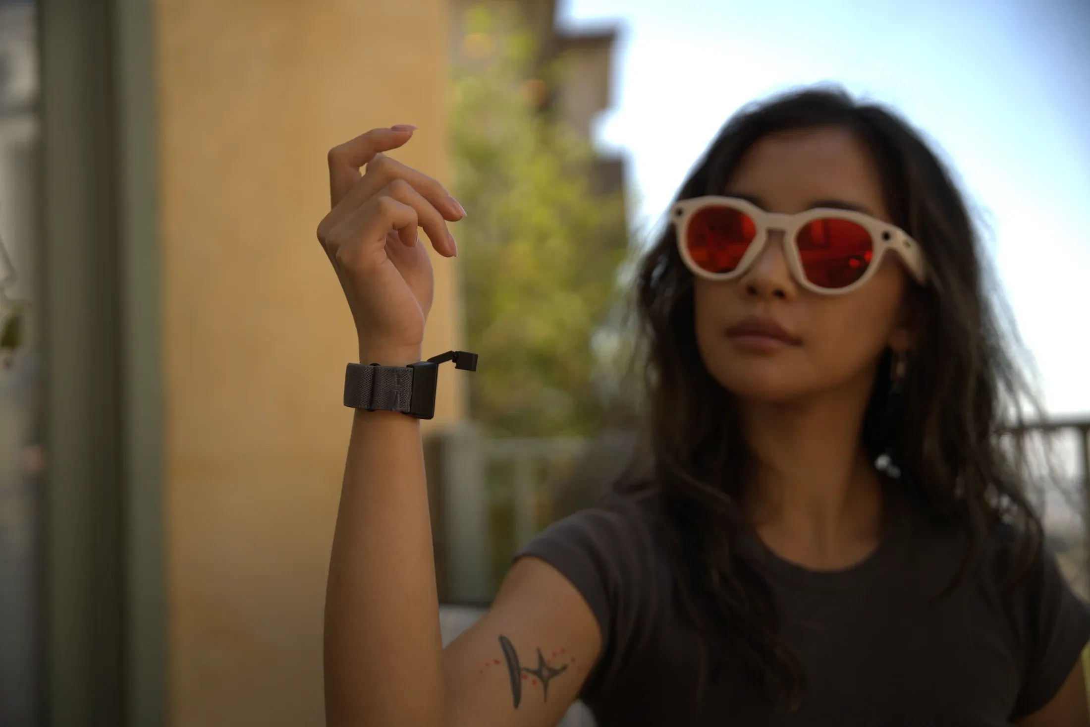 Creator wearing AR smart glasses outdoors, Tap band on her wrist, mid-gesture.